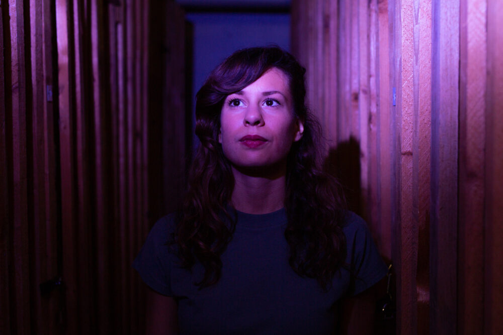 Zu sehen ist ein Portrait der Komponistin Georgia Koumará, sie ist eingetaucht in violettfarbenes Licht.